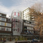 The Ora building looks almost like a regular set of apartments but with a curved, multi-colored cylindrical-shaped feature in the center.