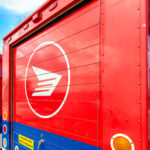 Canada Post trucks are parked under a bright blue sky.