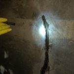 A hand in a yellow rubber glove is holding a flashlight up to a crack found in the concrete tanks of the Cameron LNG plant.