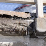 Close-up of concrete structure showing cracks and exposed reinforcing steel corroded by saltwater ingress.